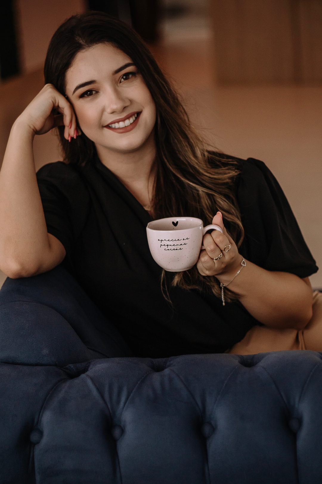Psicóloga Kamila da Silveira. Uma mulher de cabelos longos, sentada em uma poltrona azul, sorrindo e segurando uma xícara de café.